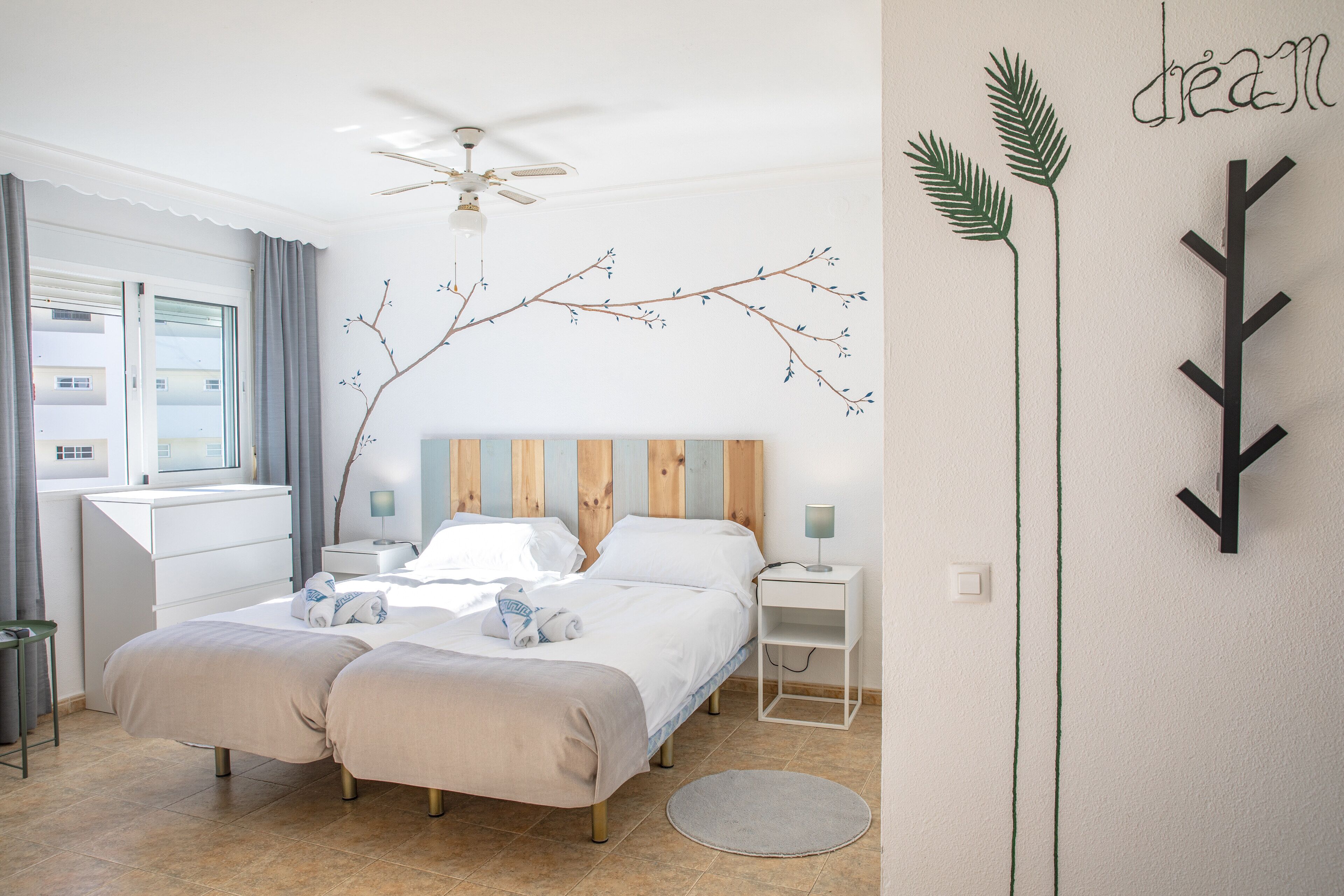 Une chambre avec deux lits, un ventilateur de plafond, une décoration murale en forme de branche et un lit avec un oreiller et une serviette.