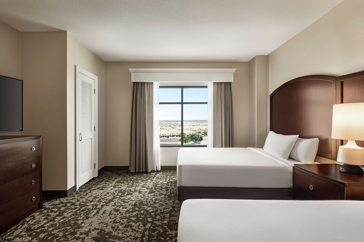 Habitación de hotel con dos camas, televisión, cómoda y ventana con vistas.