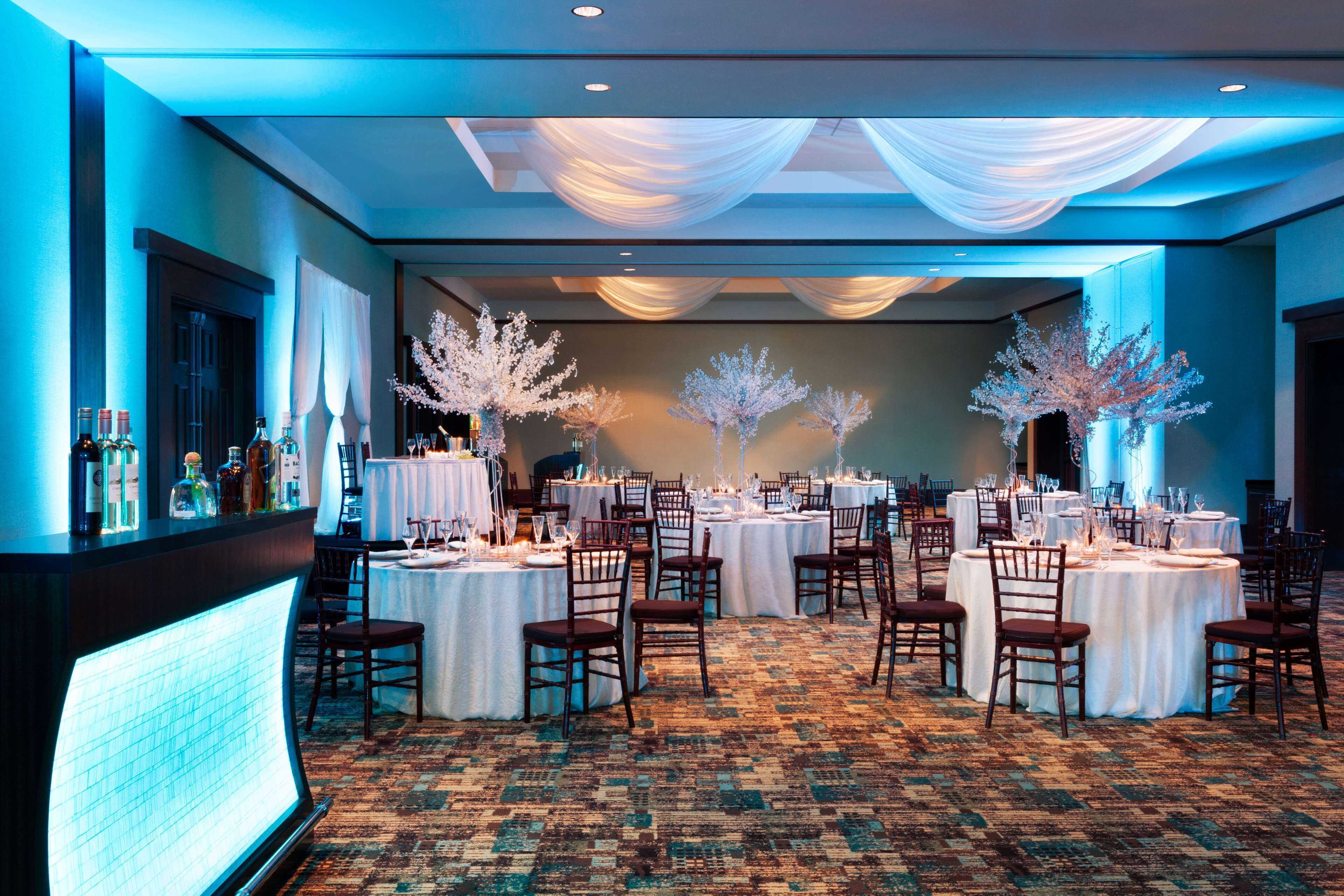 Een feestzaal met ronde tafels gedekt voor een diner, bedekt met witte stof en versierd met witte bloemstukken.