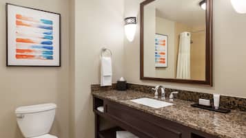 A bathroom with a white toilet, a granite countertop sink, a large mirror, and a framed abstract painting on the wall.