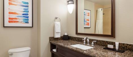 A bathroom with a white toilet, a granite countertop sink, a large mirror, and a framed abstract painting on the wall.