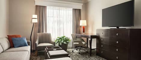 Habitación de hotel con sofá, sillón, escritorio, cómoda y televisor.