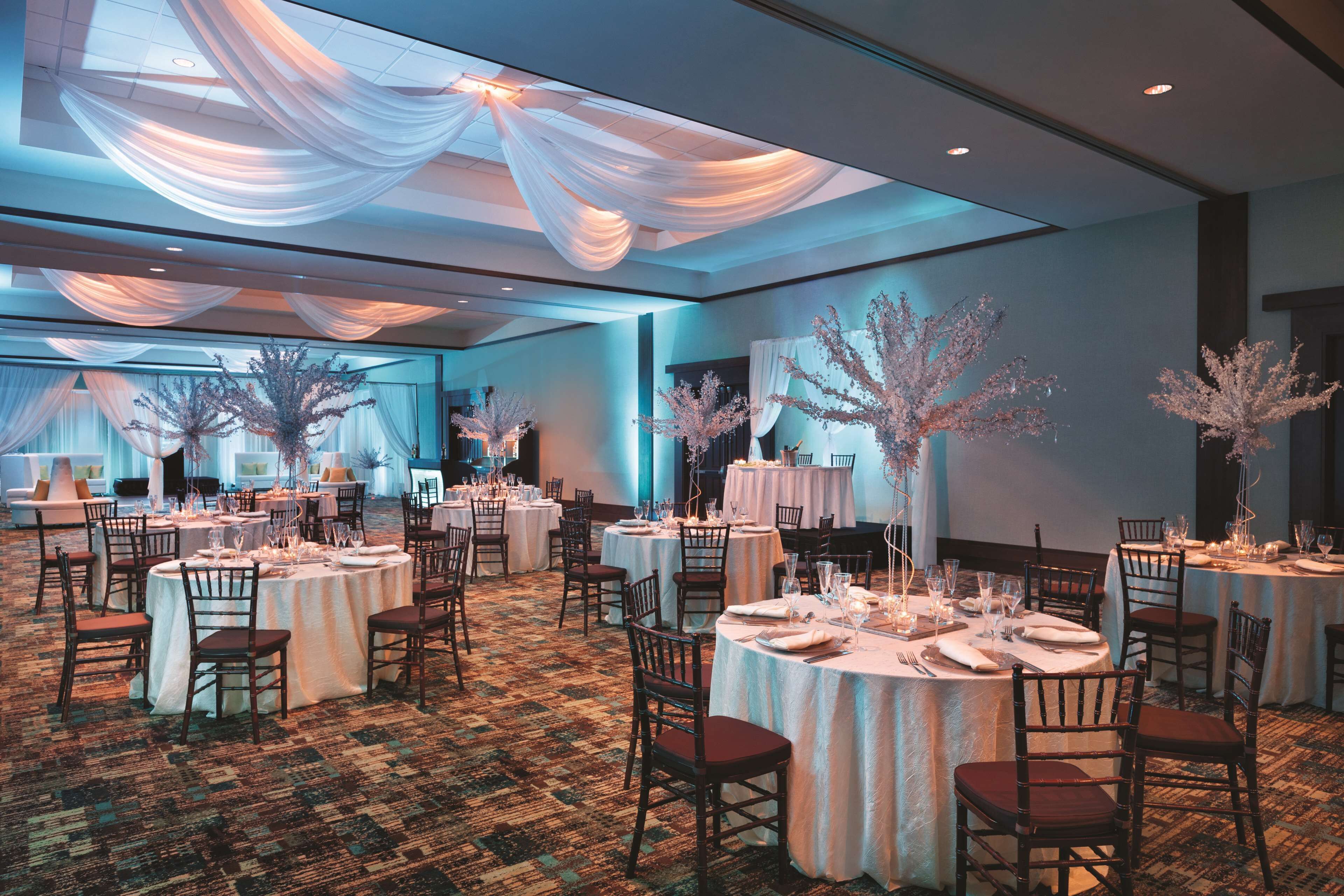Ein Festsaal mit runden Tischen, gedeckt für ein Essen, mit weißem Stoff drapiert und mit floralen Arrangements dekoriert.