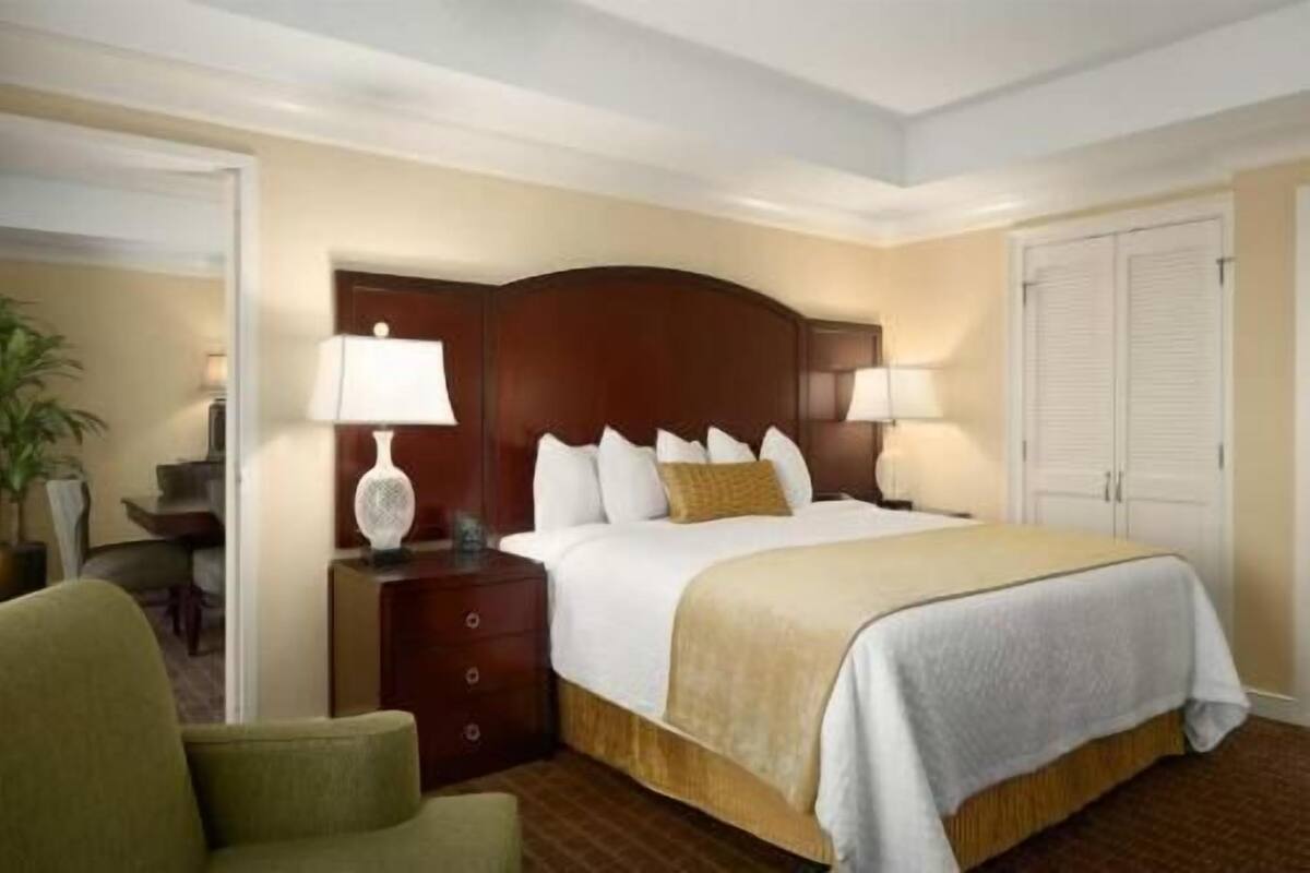 Una habitación de hotel con cama, mesita de noche, lámpara, silla y puerta.