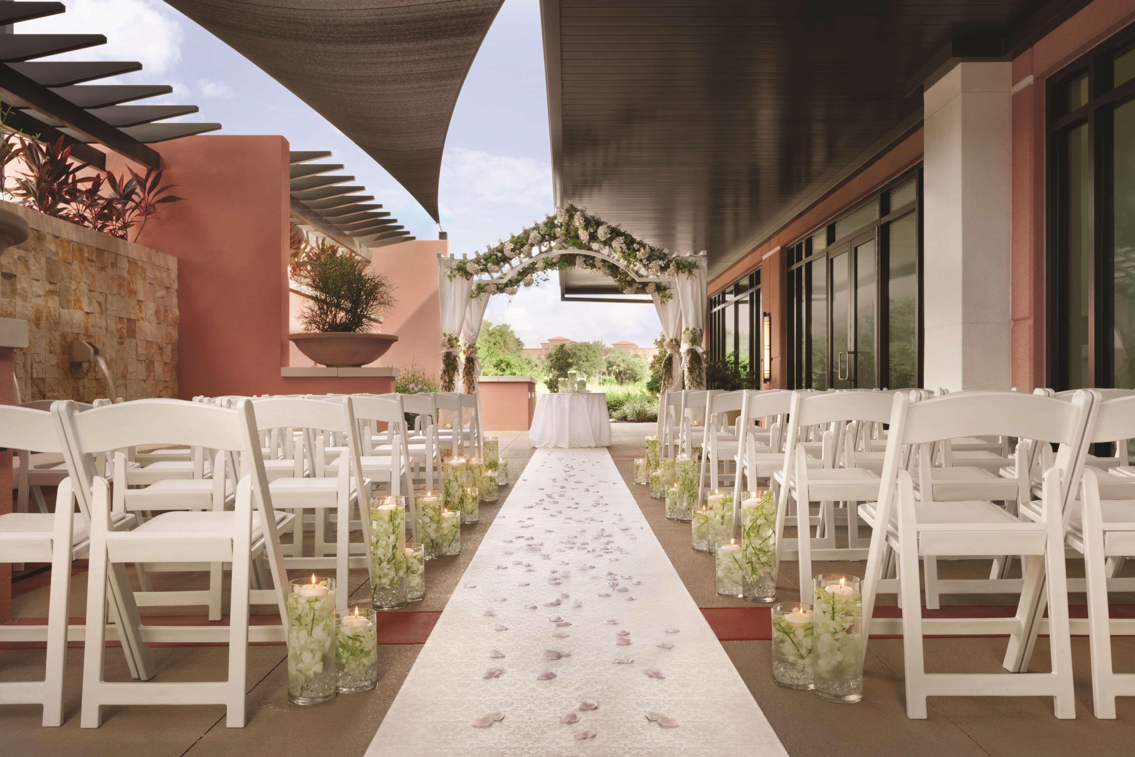 Une allée pour cérémonie de mariage en plein air, avec des chaises blanches et un tapis de fleurs.