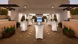 A spacious outdoor area with multiple white tables and planters, a central digital display, and a modern architectural design. - Embassy Suites by Hilton Orlando Lake Buena Vista South (Kissimmee)