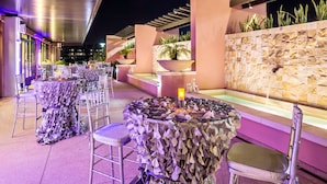 An outdoor dining area with round tables covered in foliage, surrounded by chairs, and a stone wall with plants. - Embassy Suites by Hilton Orlando Lake Buena Vista South (Kissimmee)