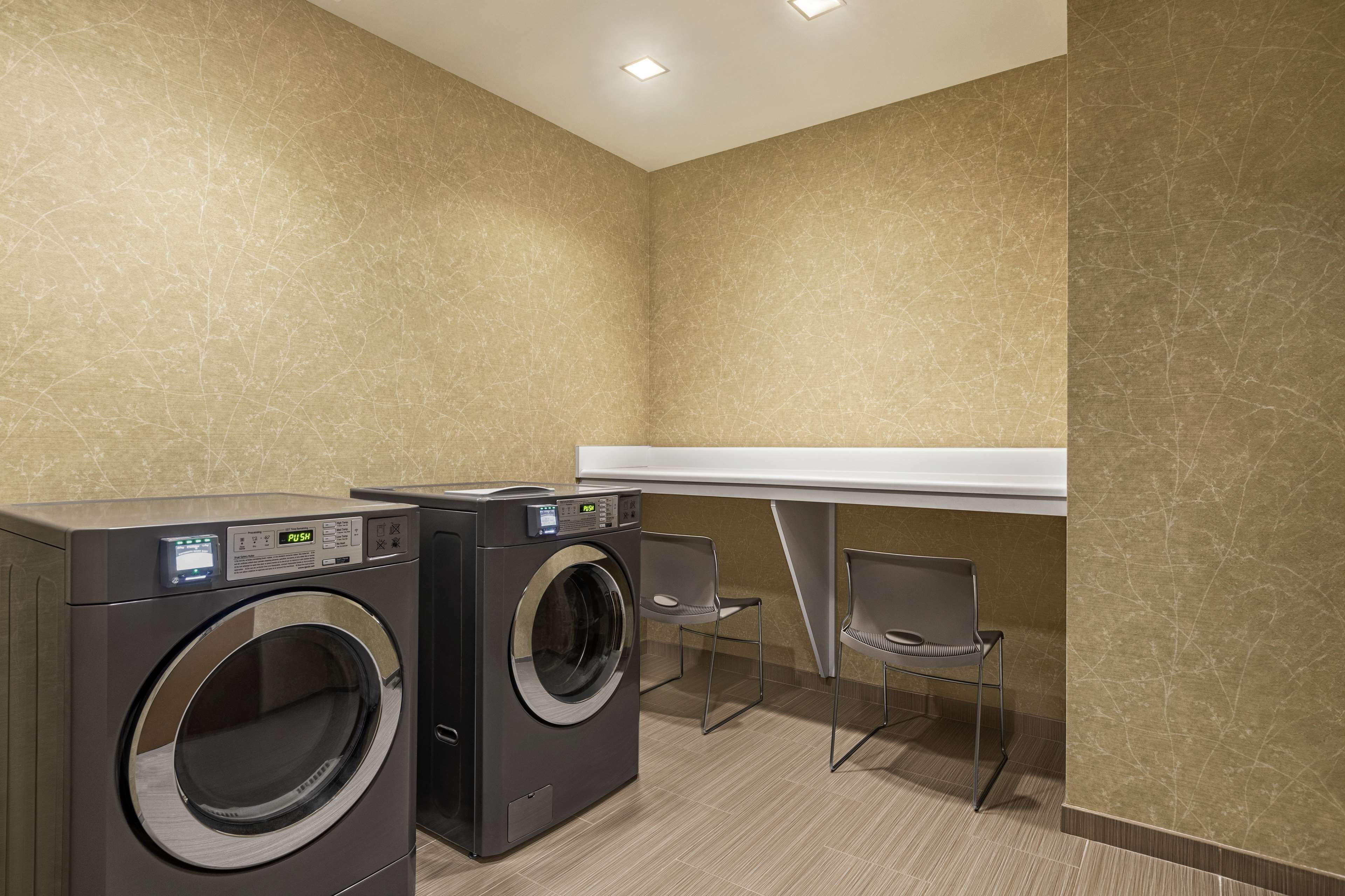 A laundry room with two front-loading washing machines, a white counter, and two chairs.