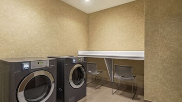 A laundry room with two front-loading washing machines, a white counter, and two chairs.