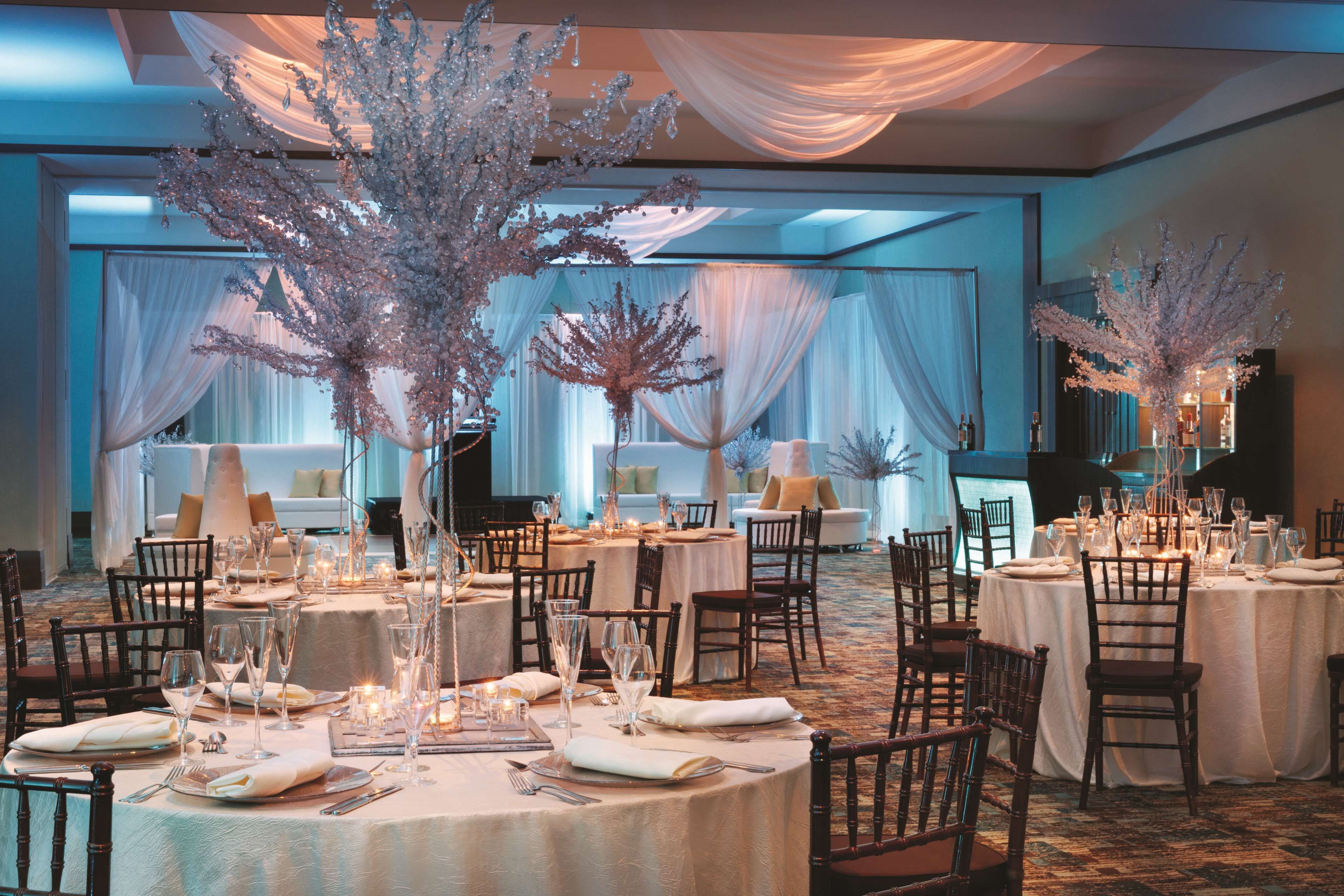 A banquet hall with round tables set for dining, draped with white linens, and decorated with floral arrangements.