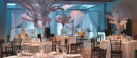 A banquet hall with round tables set for dining, draped with white linens, and decorated with floral arrangements.