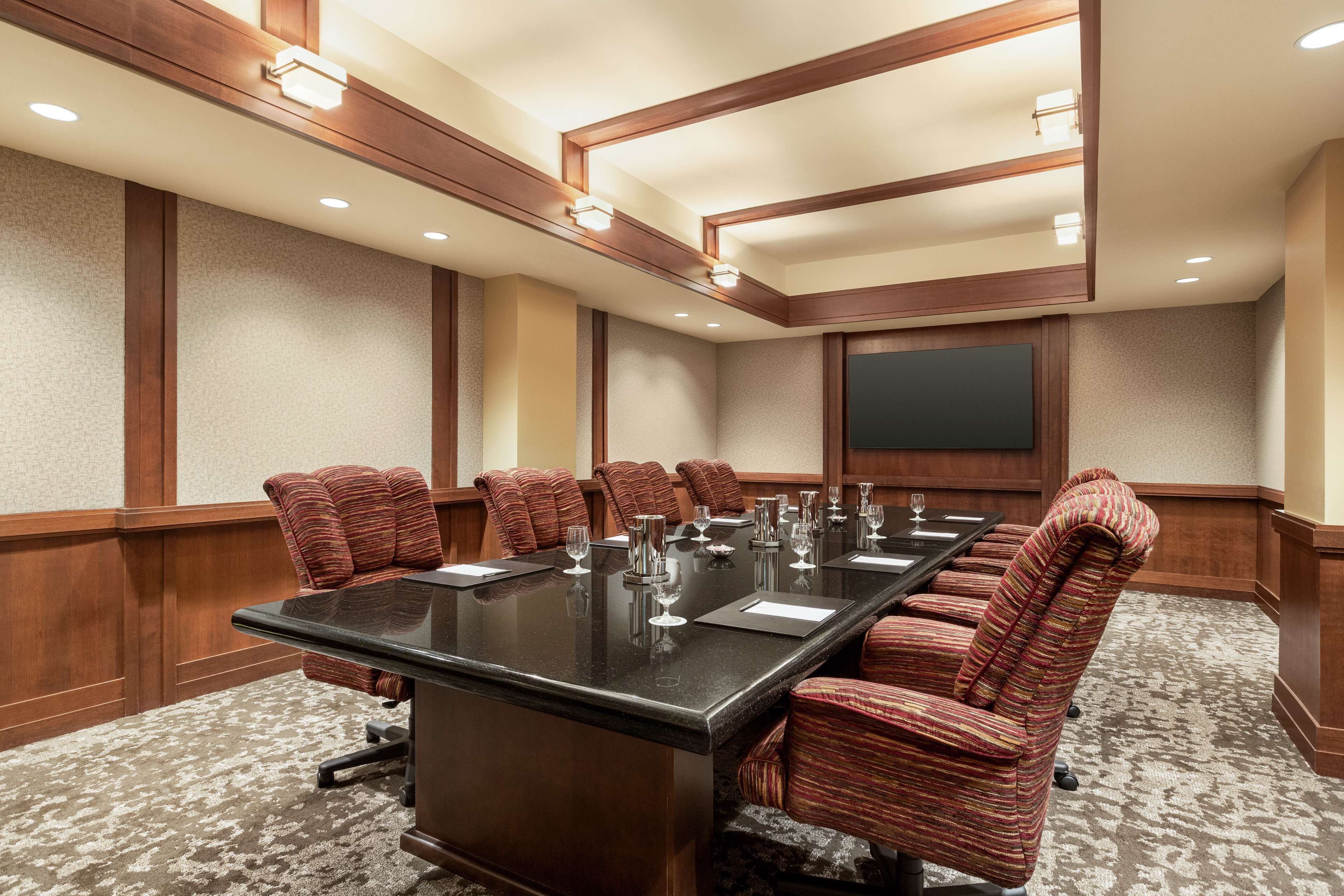 A conference room with a long table, multiple chairs, and a large screen.