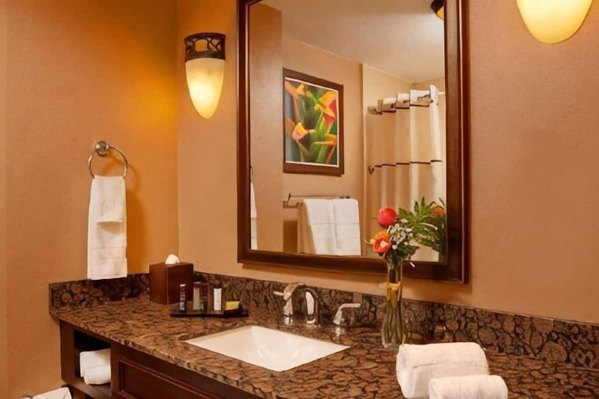 Ein Badezimmer mit Waschbecken, Spiegel, Handtuchhalter und einer Vase mit Blumen.
