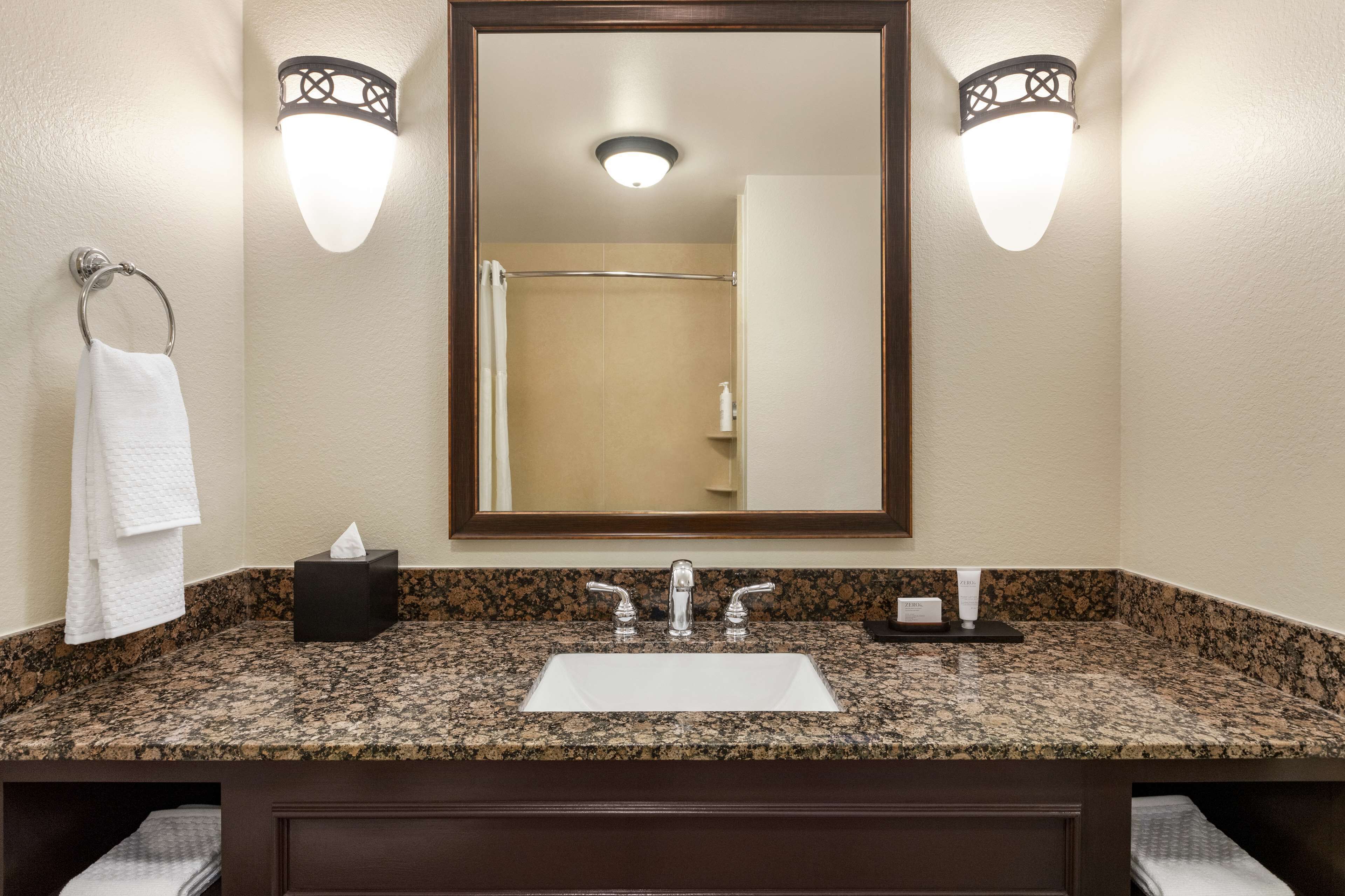 A bathroom with a granite countertop, a white sink, two wall-mounted lights, and a mirror above the sink.
