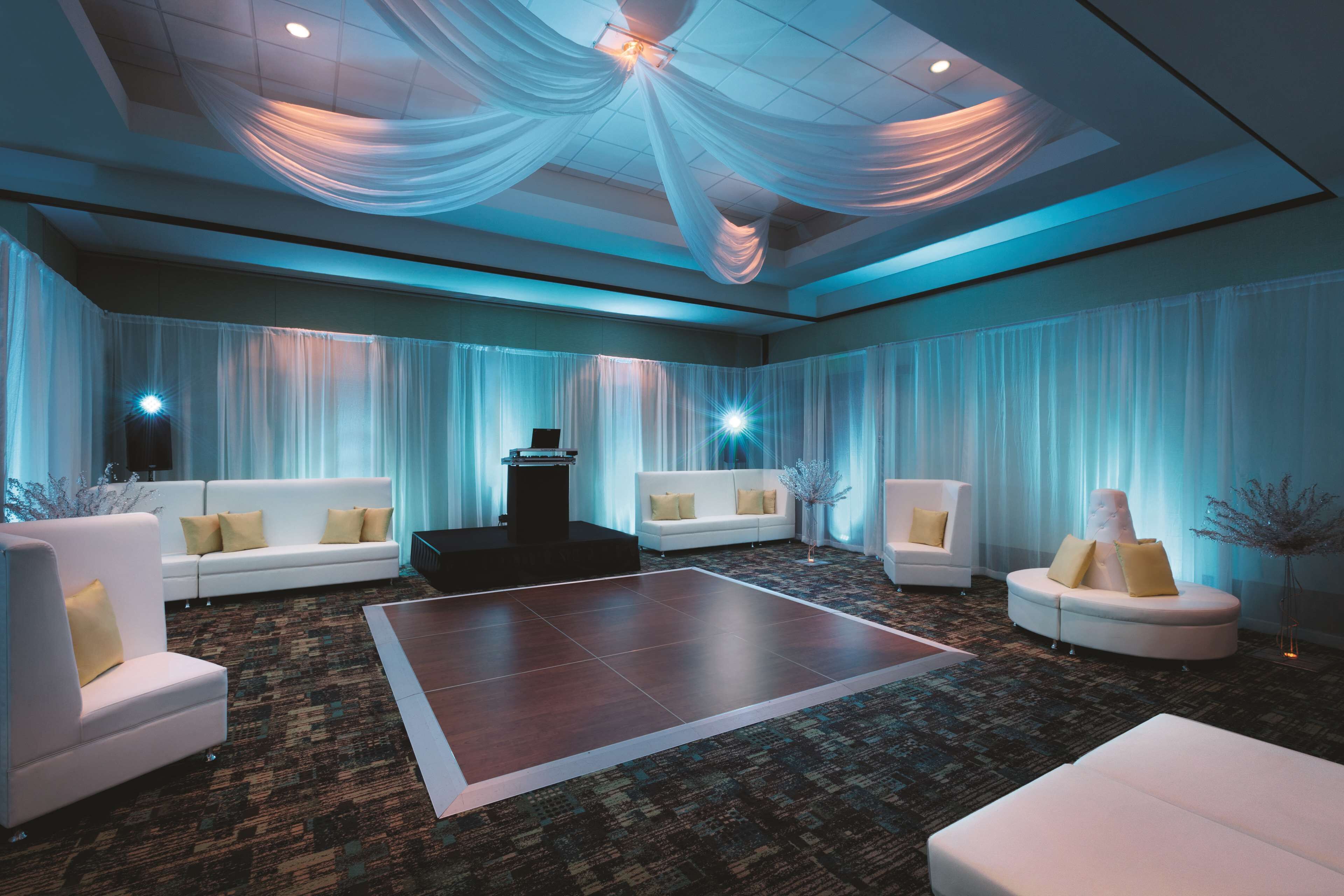 A spacious room with a large dance floor, white sofas with yellow cushions, and a stage with a podium.