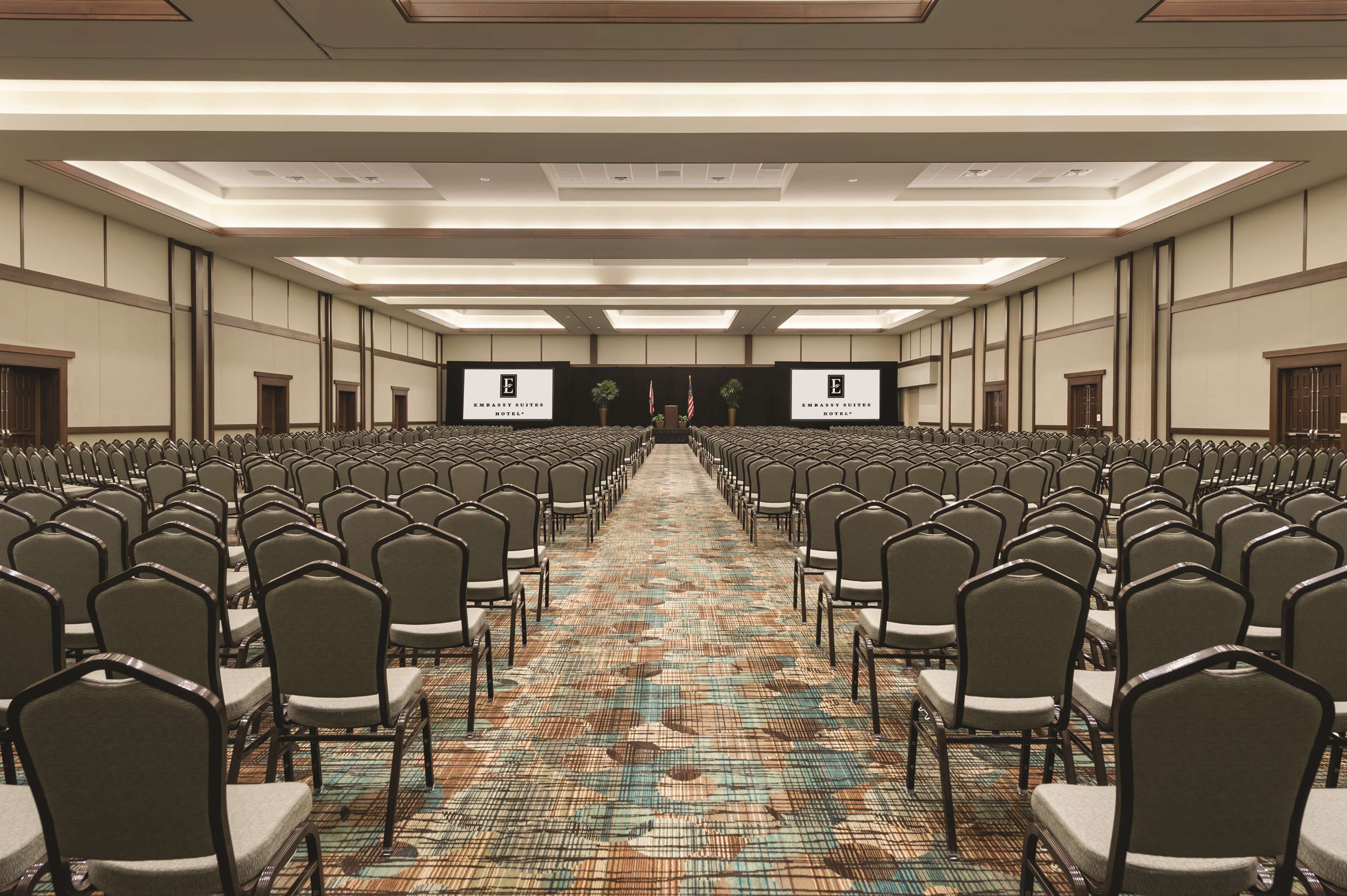 A conference room with rows of chairs and tables, a patterned carpet, and a ceiling with recessed lighting.