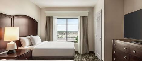 A hotel room with two beds, a television, a dresser, and a window with curtains.