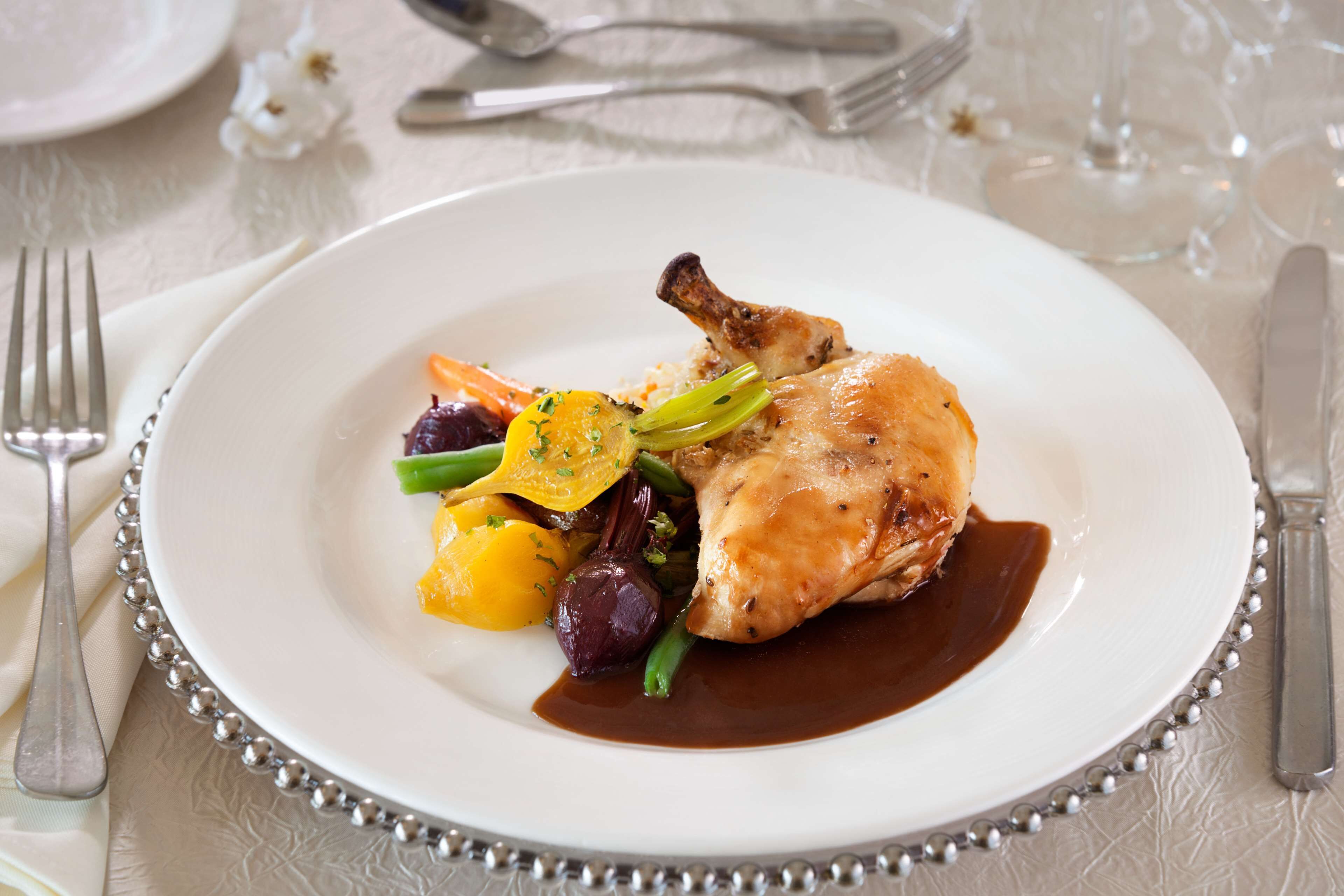 A white plate with a roasted chicken leg, vegetables, and sauce.
