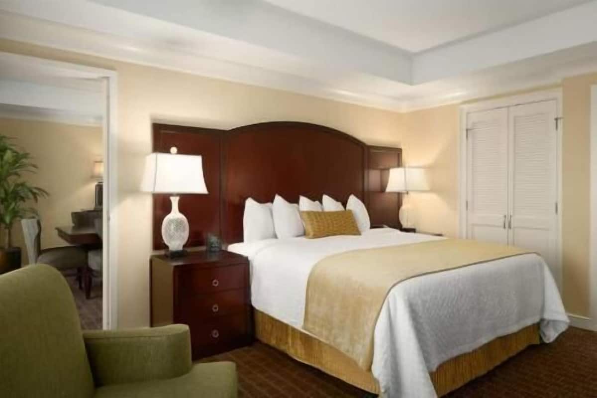 Una habitación de hotel con cama, mesita de noche, lámpara, silla y puerta.
