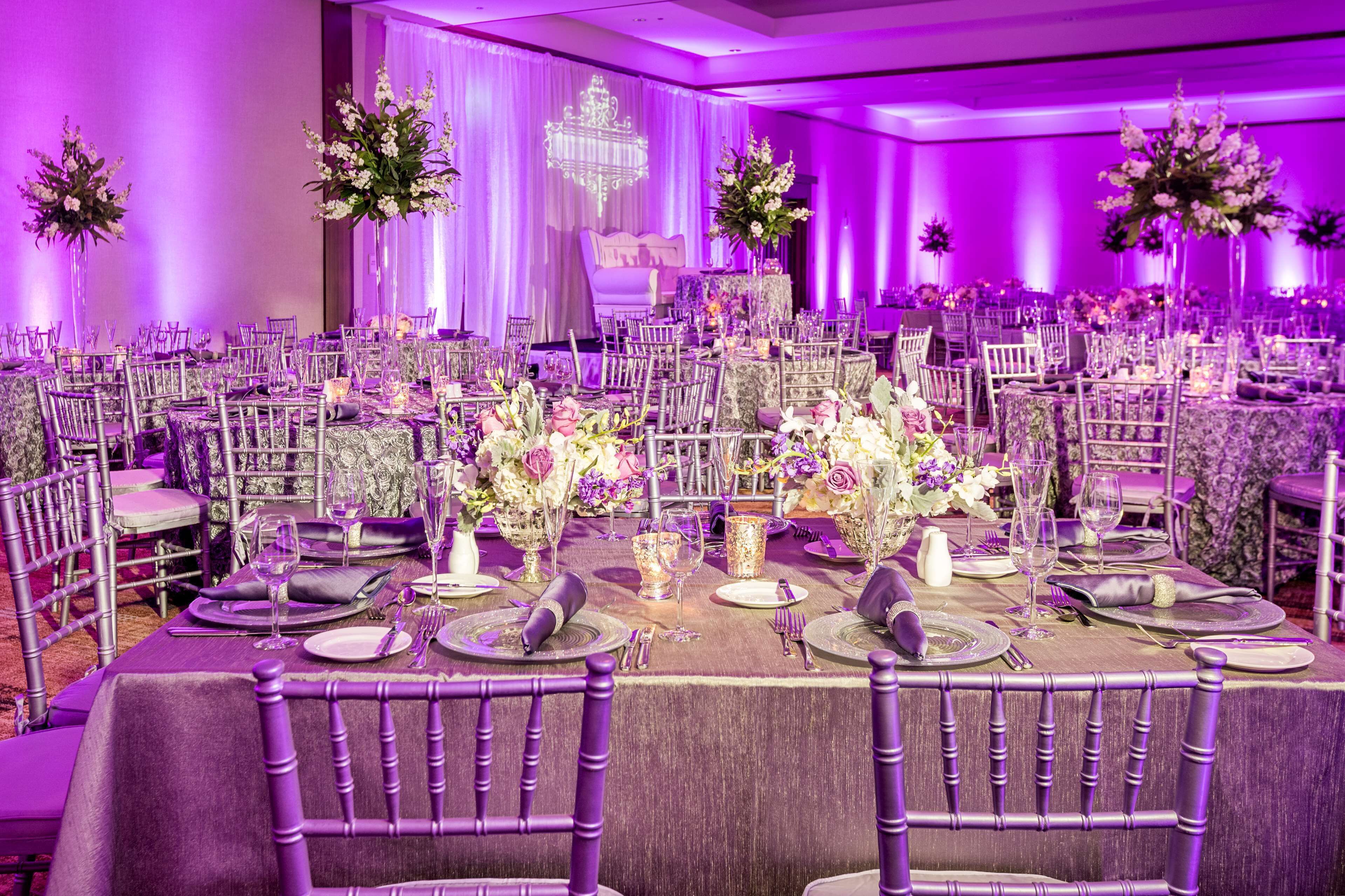 A banquet hall with round tables, purple chairs, and floral centerpieces.