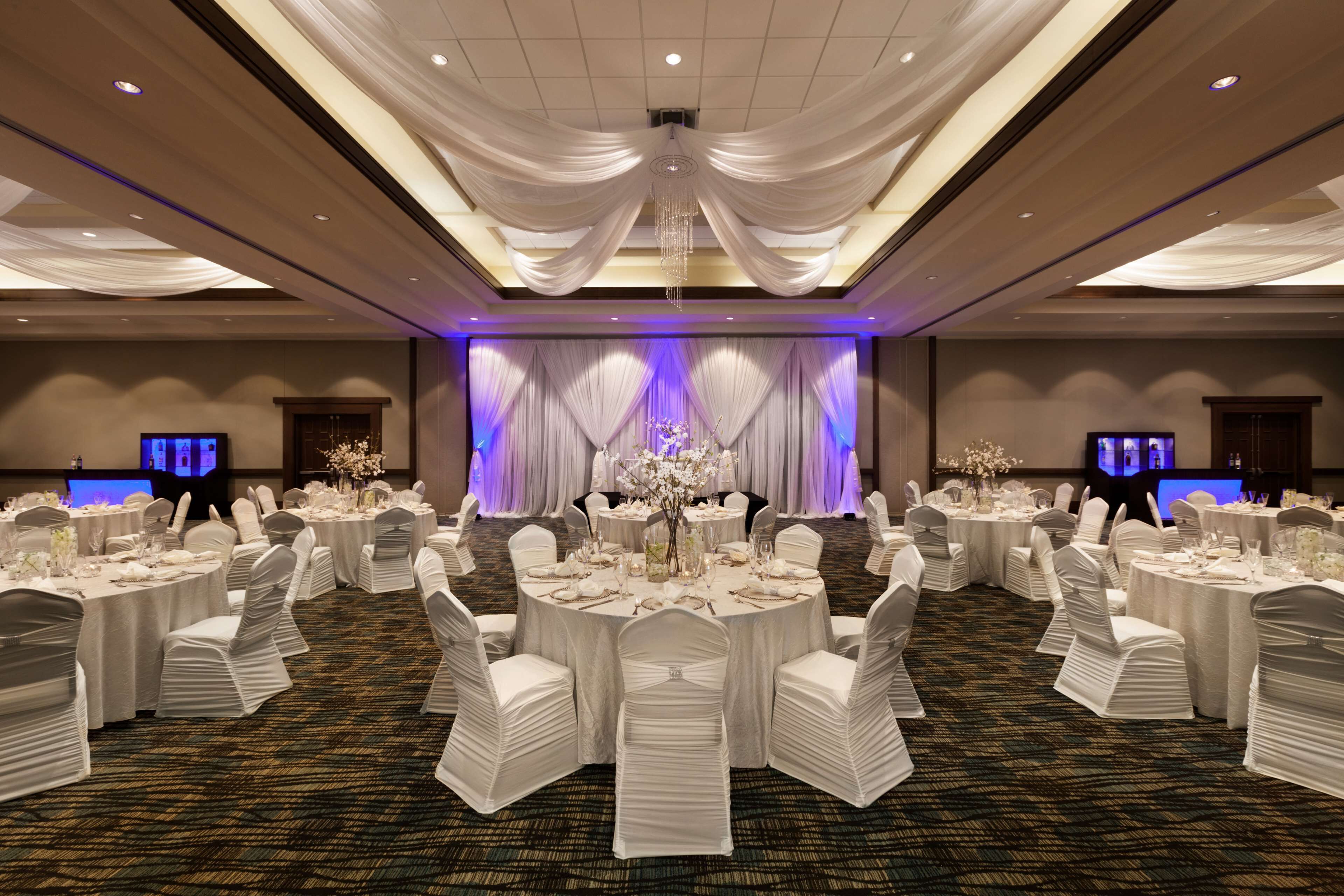 A banquet hall with round tables, white chairs, and draped curtains.