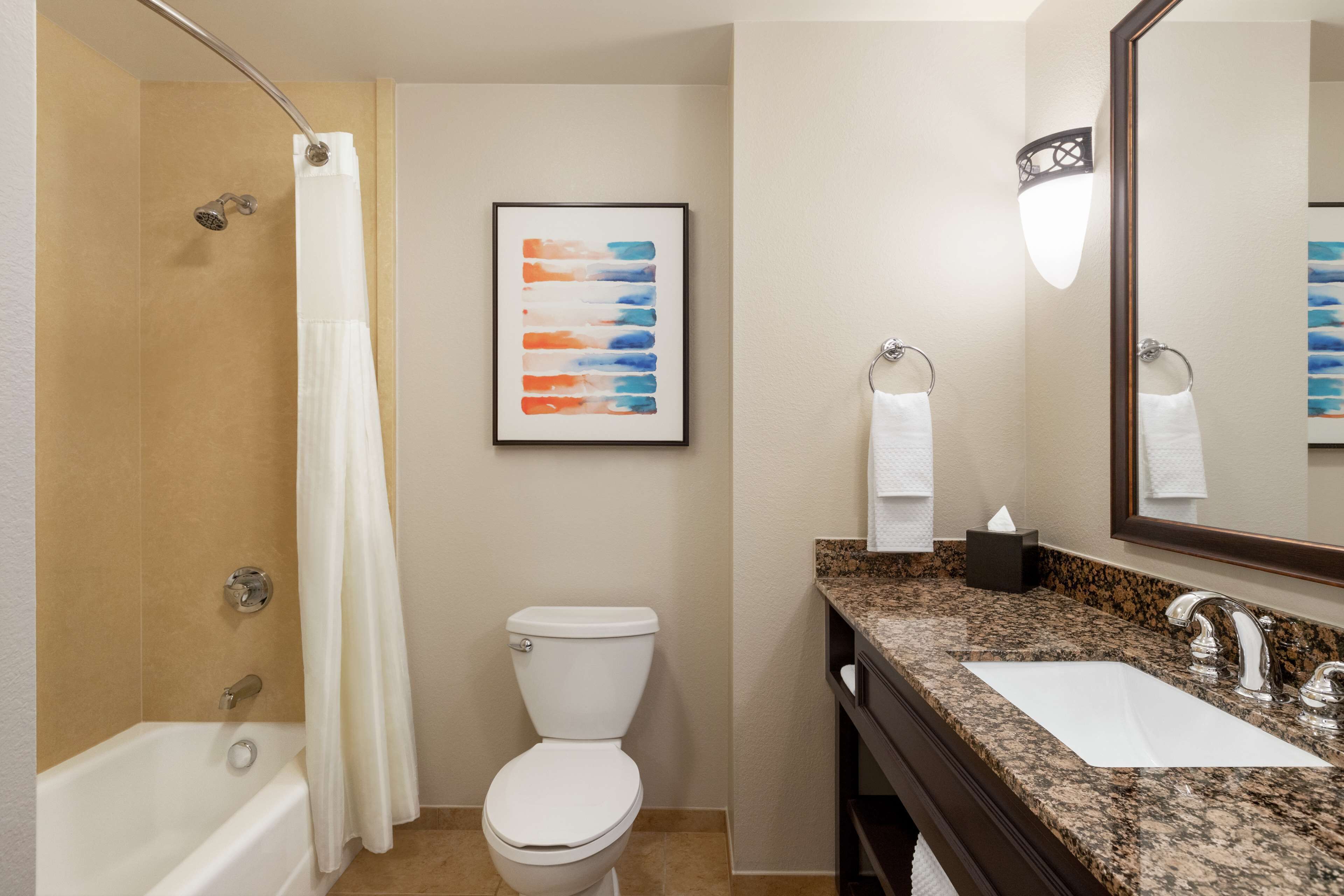 A bathroom with a bathtub, toilet, sink, and a framed abstract painting.