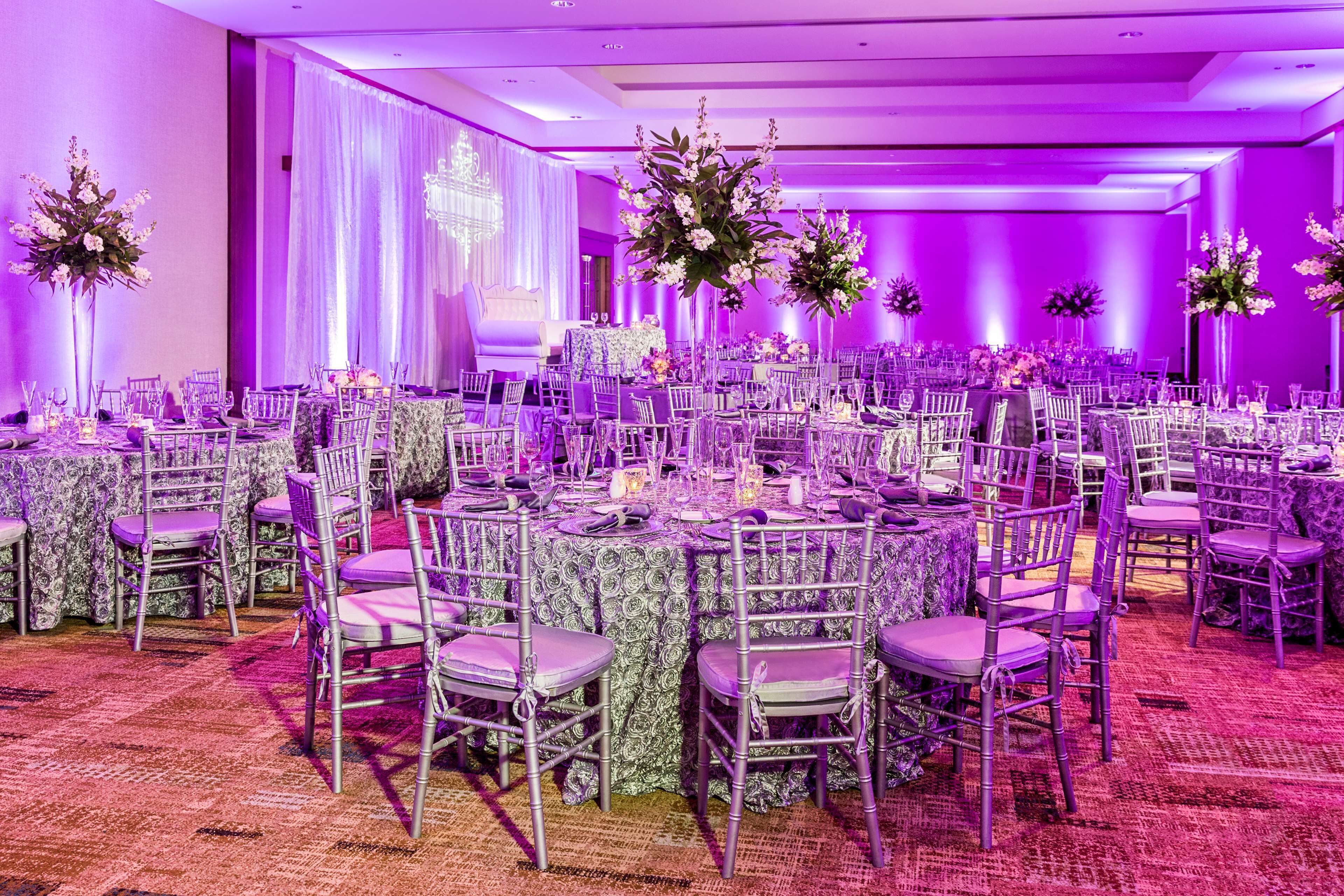 Un salón de banquetes con mesas redondas, sillas y centros de mesa florales.