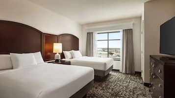Habitación de hotel con dos camas, un ventanal con cortinas, un aparador y un televisor.