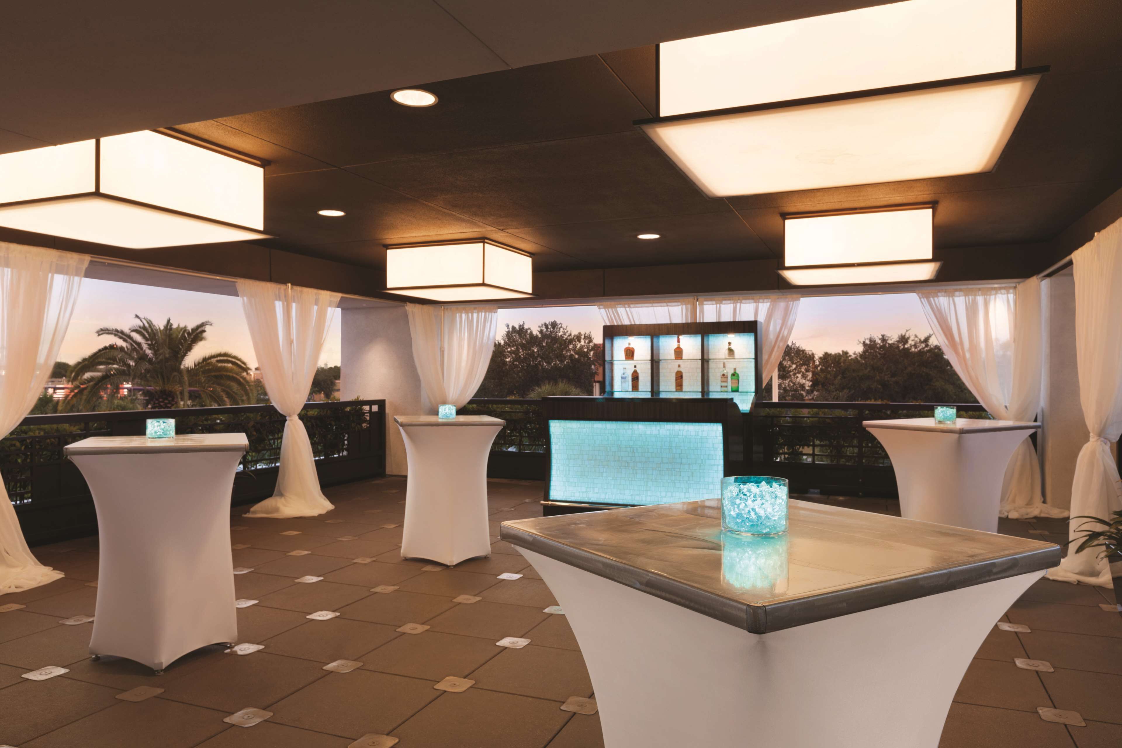 A terrace with white tables and chairs, a bar area, and a view of palm trees.