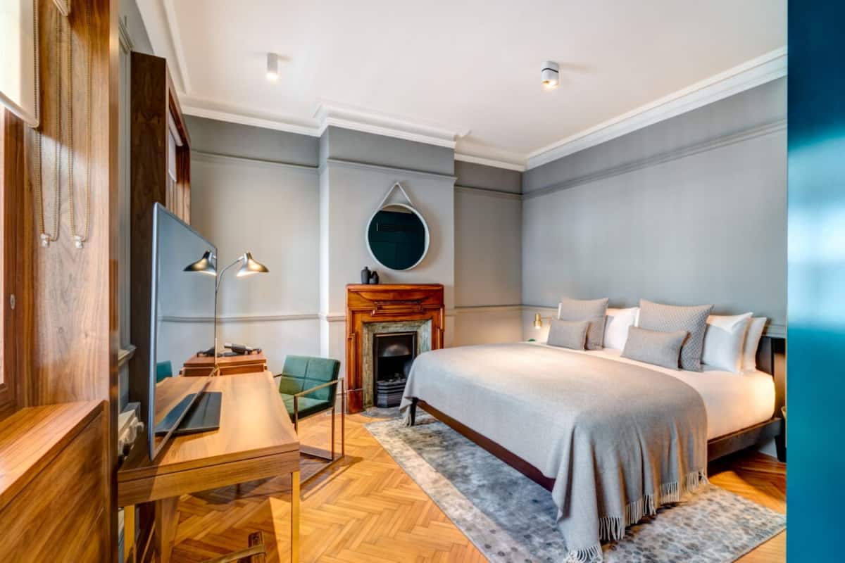 A modern bedroom with a large bed, a fireplace, a television, and a desk.