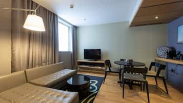 A modern hotel room with a sofa, a coffee table, a TV, and a dining area with chairs and a small table.
