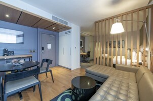 Ein modernes Hotelzimmer mit Essbereich, einer Couch, einem runden Couchtisch und einem Schreibtisch.