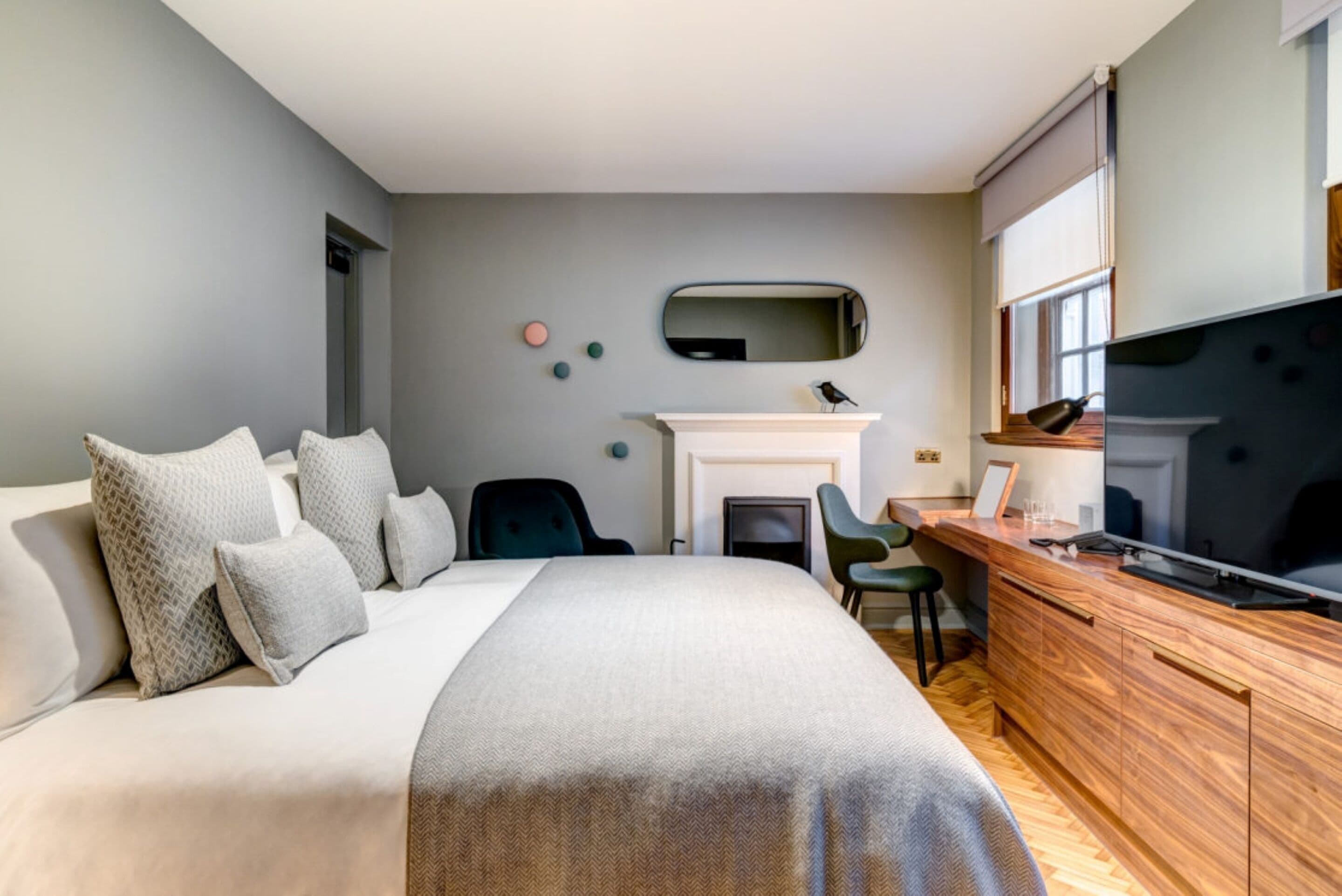 A modern hotel room with a large bed, a wooden desk, a television, and a fireplace.