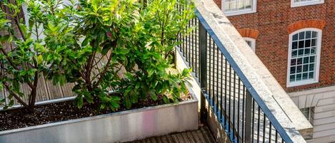 Una terraza en la azotea con cubierta de madera, sillas blancas y un taburete rosa.