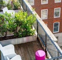 Una terrazza sul tetto con pavimento in legno, sedie bianche e uno sgabello rosa.