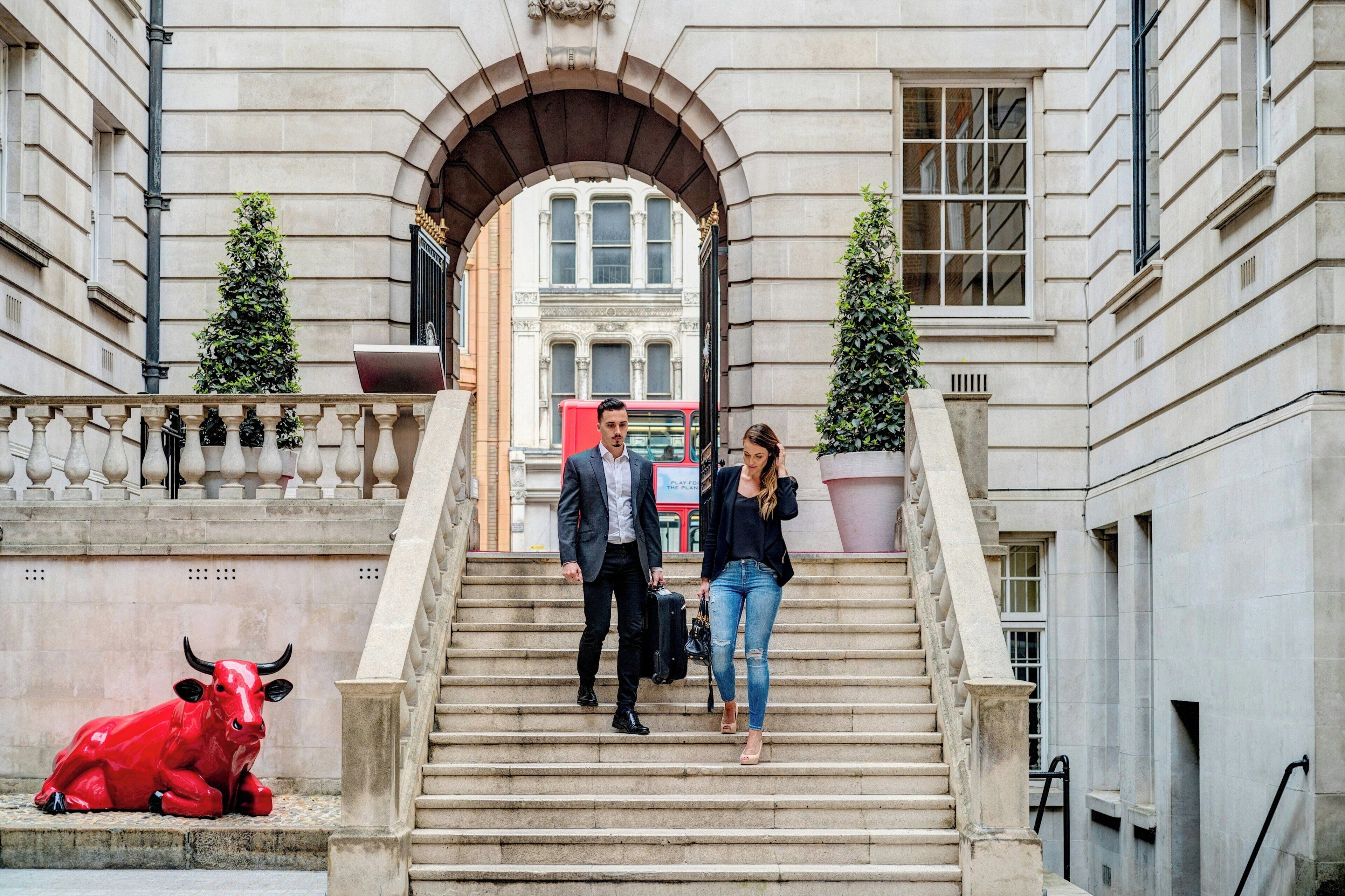 A stone staircase with a bull sculpture at the bottom, leading to a building with a large arched entrance.
