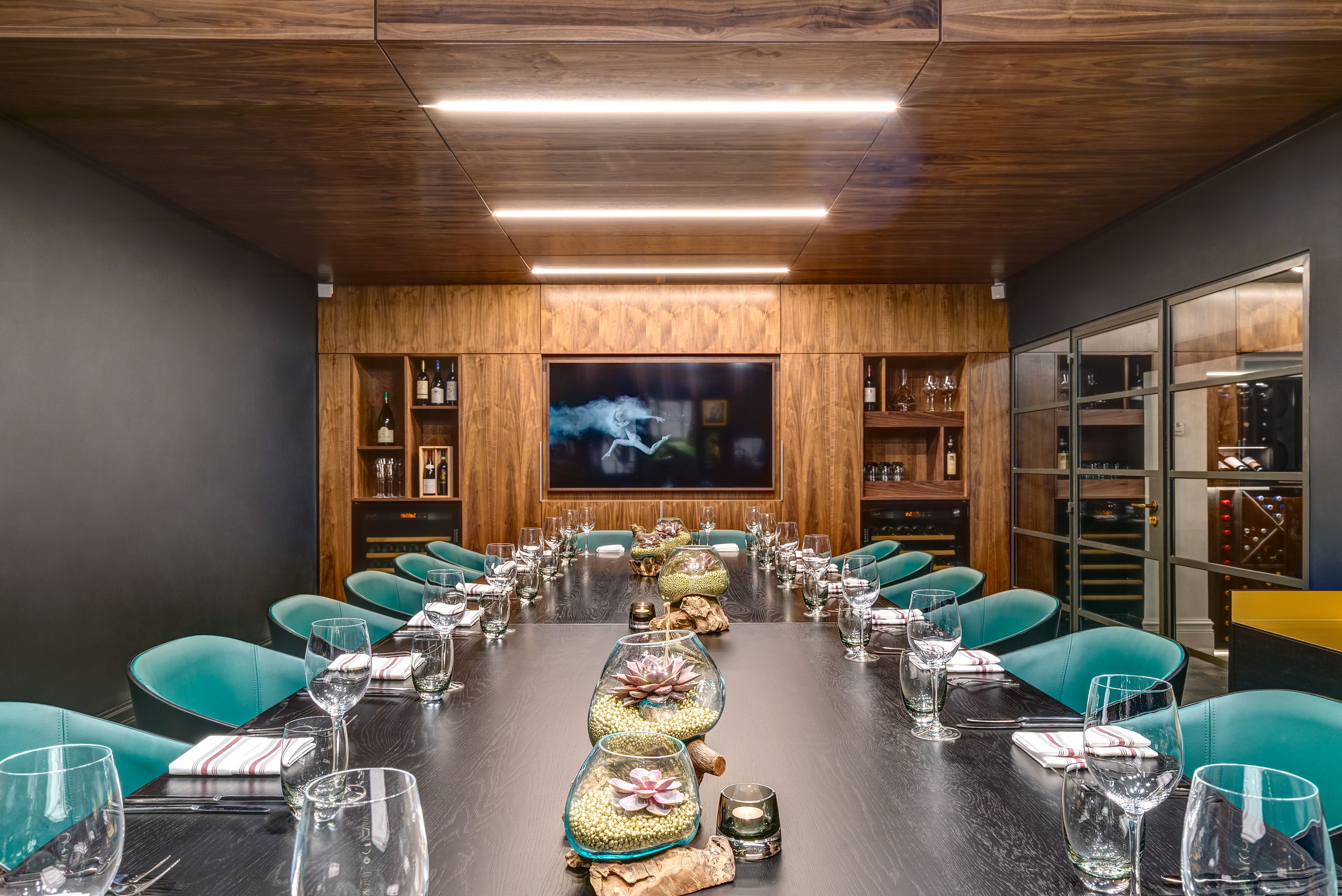 A conference room with a long table, teal chairs, and a large screen.
