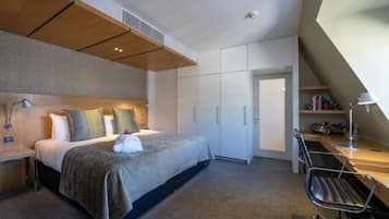 Una habitación de hotel moderna con una cama grande, un escritorio y una silla. Hay un armario y una puerta que da a otra habitación.