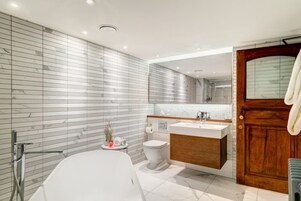 Ein modernes Badezimmer mit einer freistehenden Badewanne, einem Holzwaschtisch, einer Toilette und einem großen Spiegel.