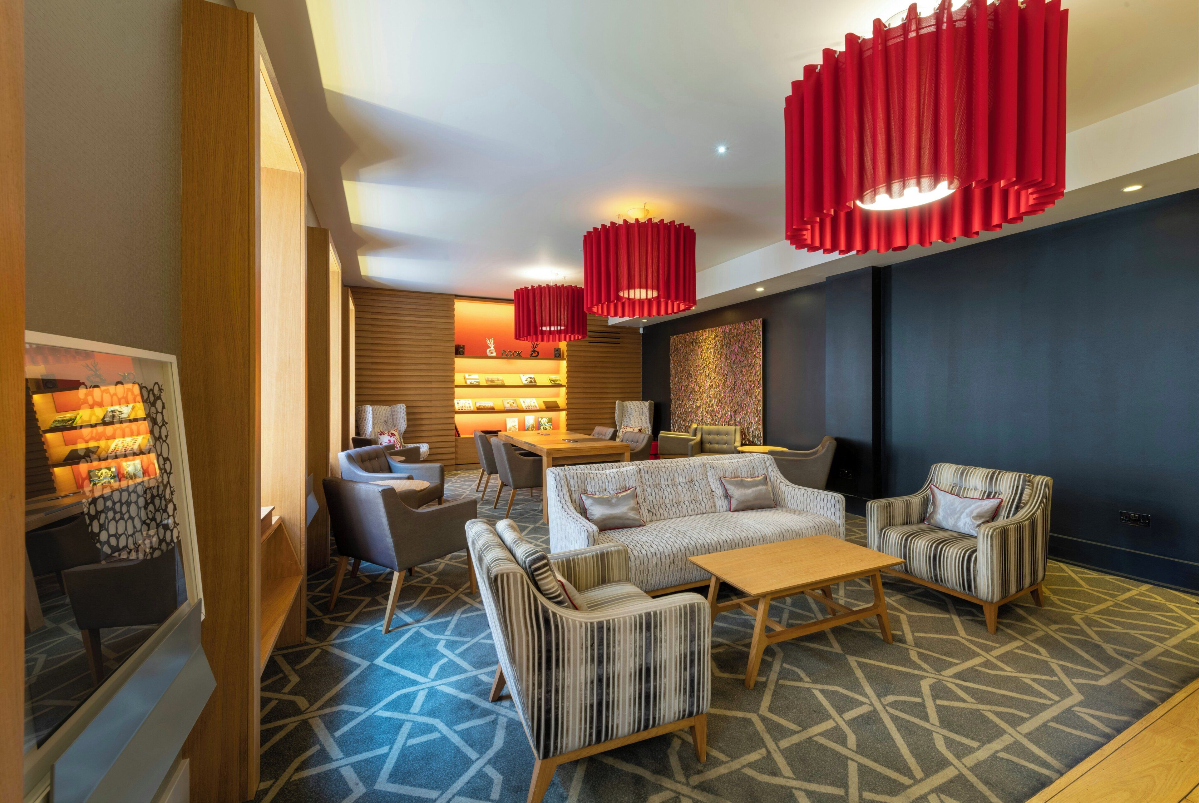 A modern lounge area with a sofa set, armchairs, a coffee table, and a bookshelf with books.