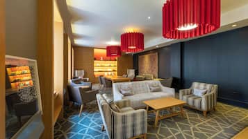 A modern lounge area with a sofa set, armchairs, a coffee table, and a bookshelf with books.