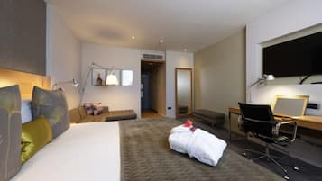 Habitación de hotel moderna con una cama grande, un escritorio con silla, un televisor de pantalla plana y un baño visible a través de una puerta abierta.