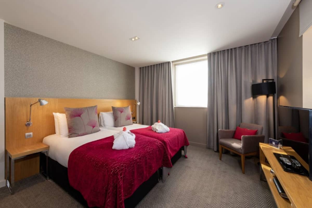 A hotel room with a large bed, two bedside tables, a desk, a chair, and a TV.
