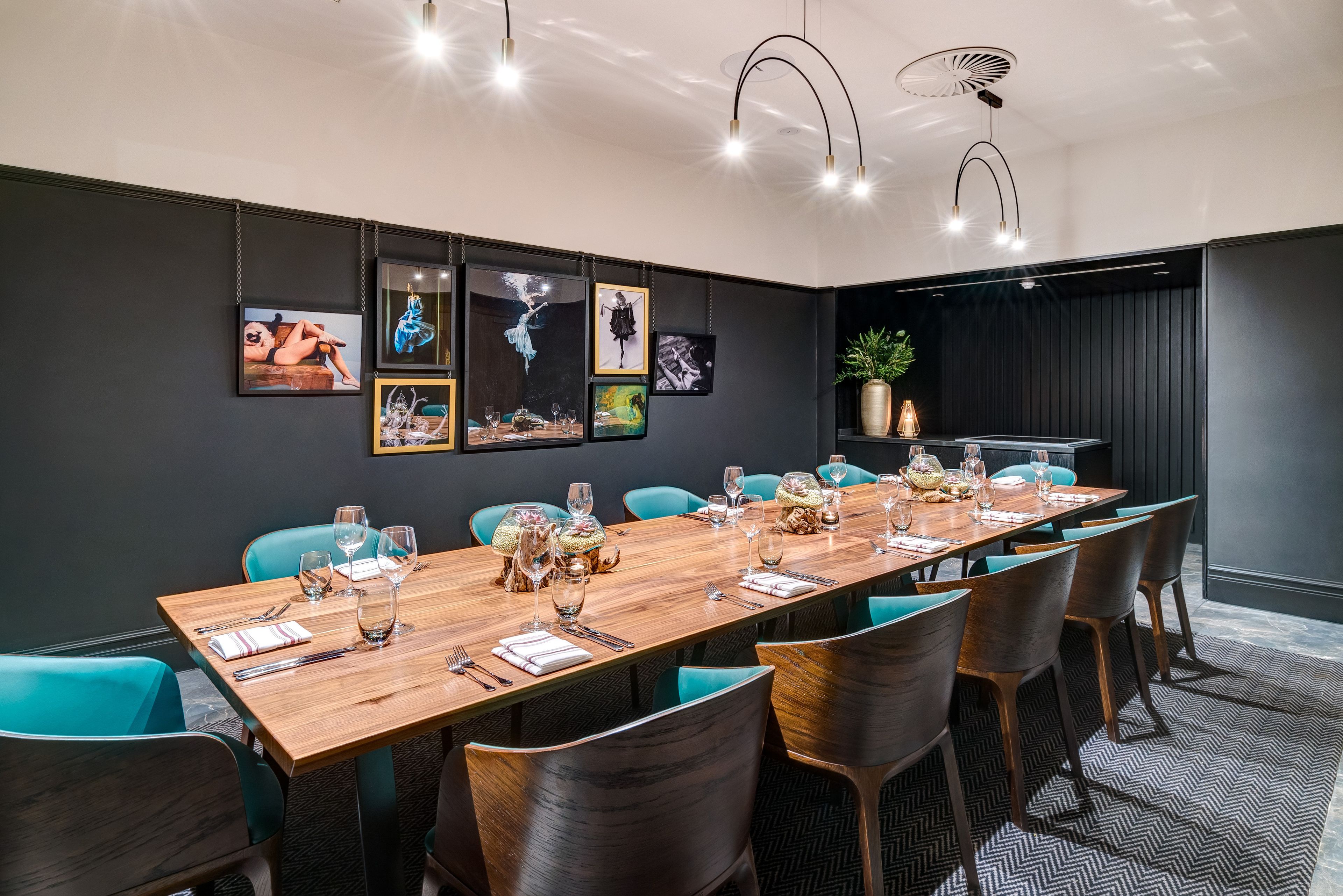 A modern conference room with a long wooden table set for a meeting, teal chairs, and framed artwork on the walls.