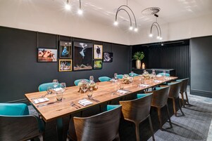 A modern conference room with a long wooden table set for a meeting, teal chairs, and framed artwork on the walls.