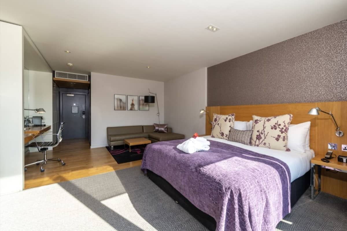 A hotel room with a bed, a desk, a chair, a sofa, and a small table.