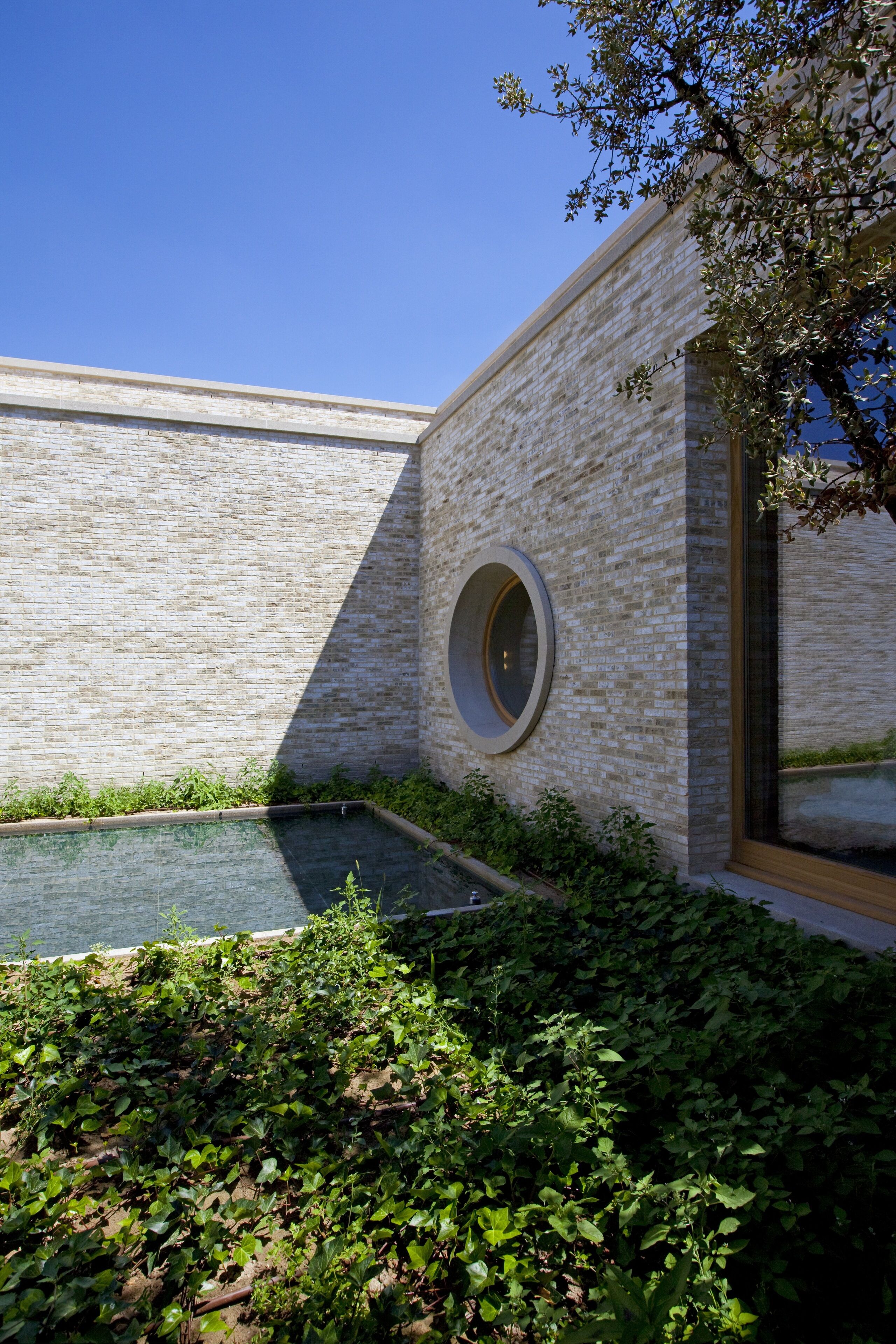 Un bâtiment moderne avec une façade en briques, une fenêtre circulaire et une petite piscine entourée de verdure.