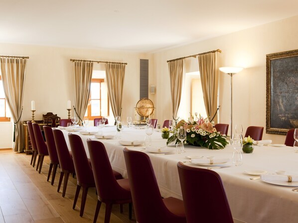 Un comedor formal con una larga mesa dispuesta para una comida, sillas rojas y un globo terráqueo como centro de mesa.