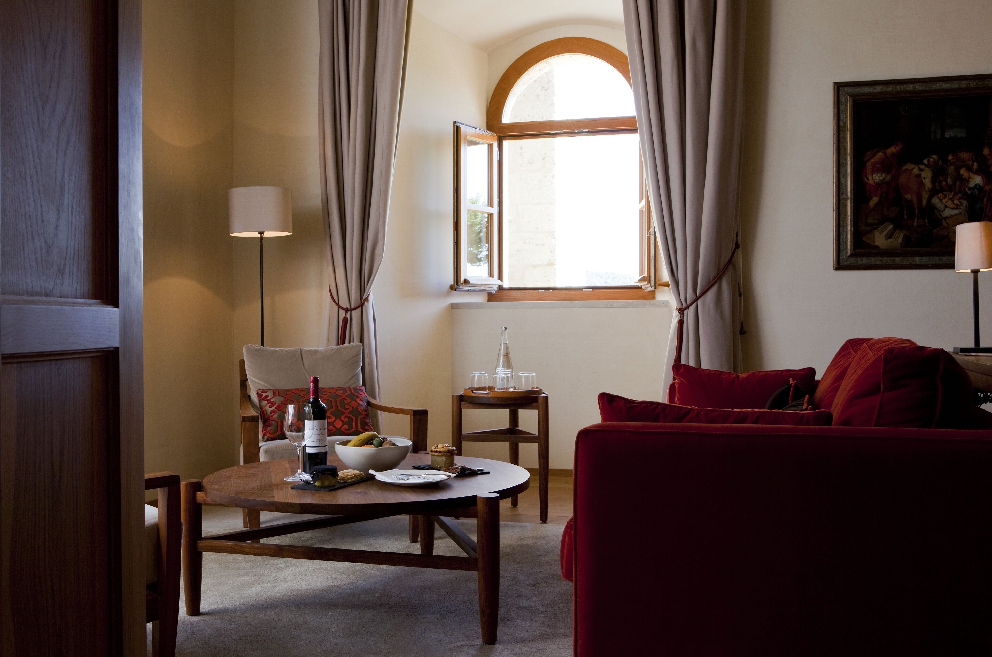 A cozy living room with a wooden table set for a meal, a red sofa, and a painting on the wall.