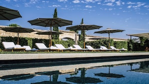 Un espace aménagé au bord de la piscine, avec des chaises longues et des parasols, un mur en pierre et un ciel dégagé.